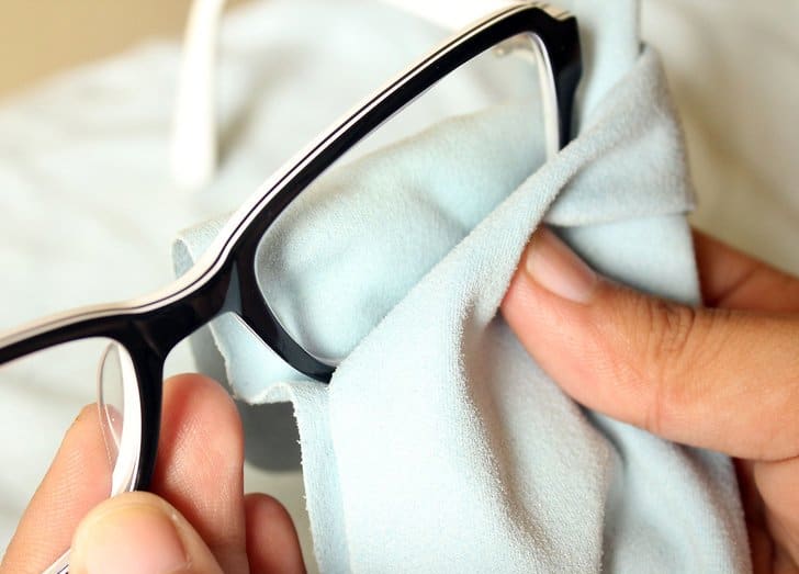 A close-up of eyeglasses being cleaned with a microfiber cloth.