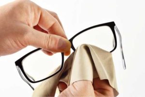 A person holding a pair of eyeglasses in one hand and using a blue microfiber cloth to clean the lenses with the other hand.