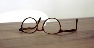 A person's hand holding a pair of eyeglasses, while the other hand is placing the glasses on a wooden table.