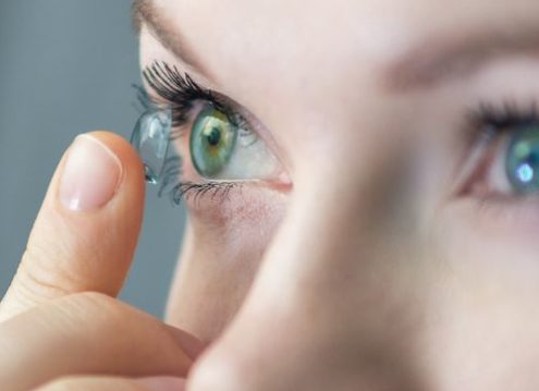 Close-up of a person inserting a contact lens into their eye with a smile.